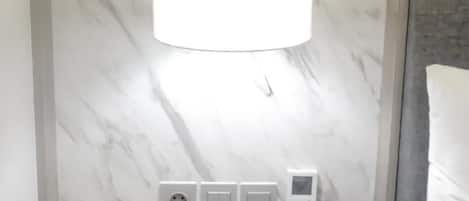 Ett modernt hotellrum med en vägg av marmor, ett sängbord med en lampa, en telefon och ett anteckningsblock.