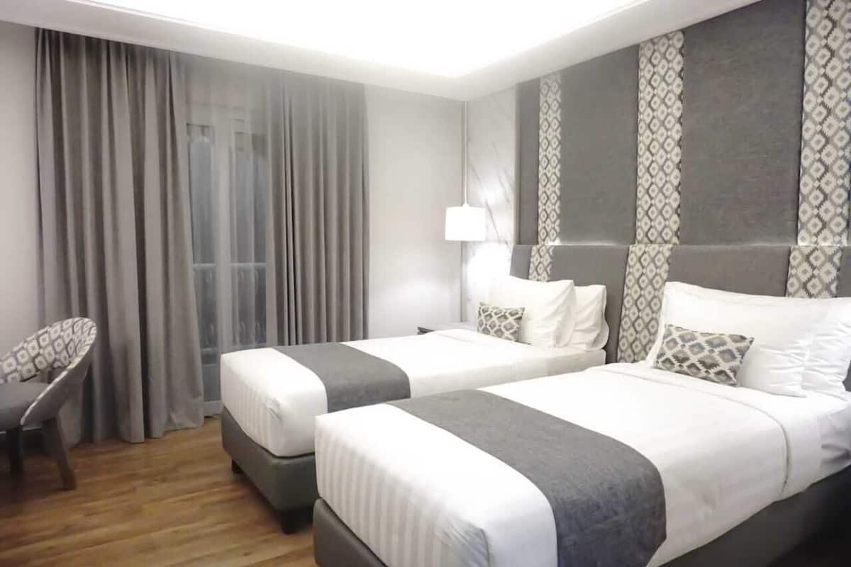 A hotel room with two beds, a chair, a lamp, and a large window with curtains.