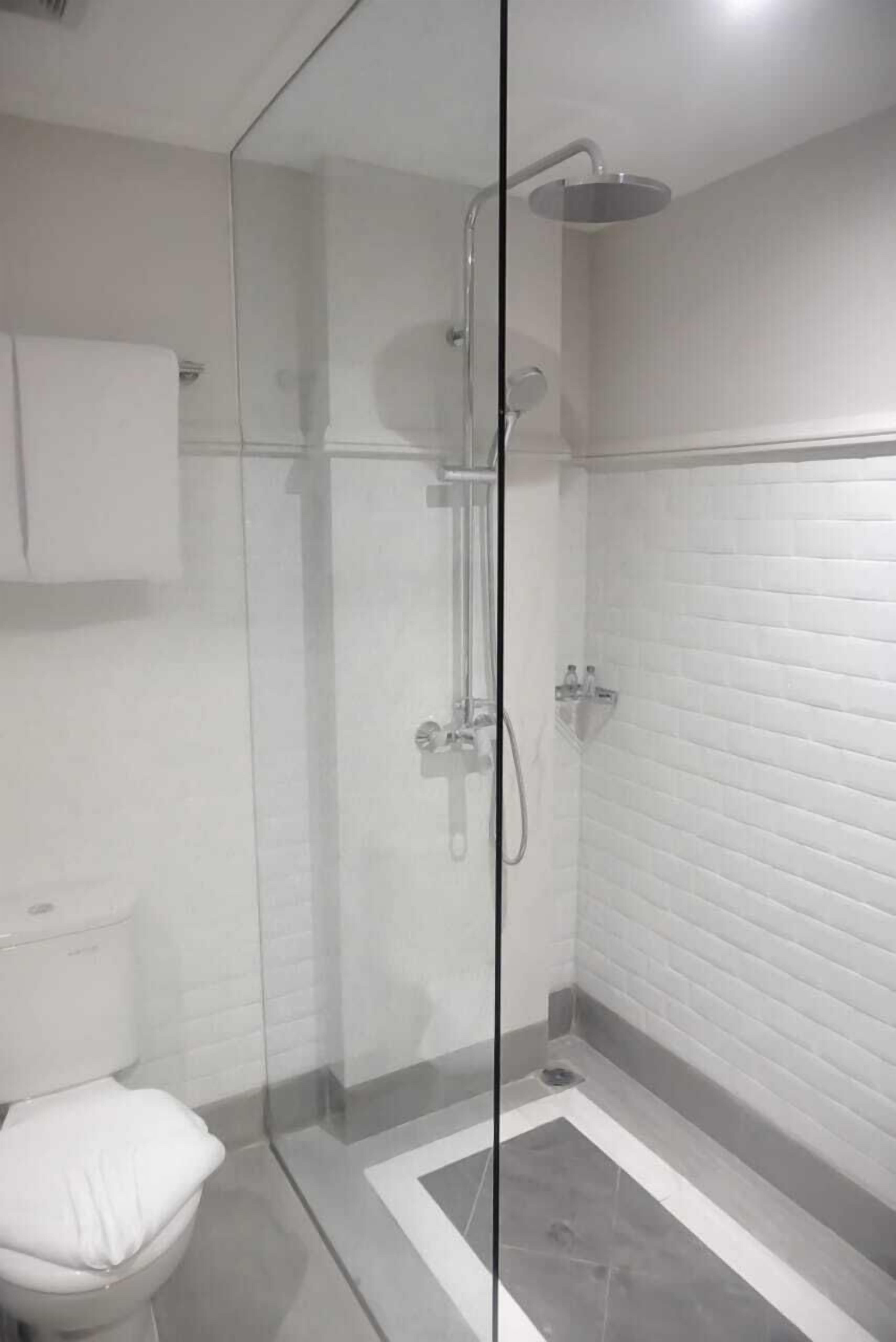 A modern bathroom with a glass-enclosed shower, white tiled walls, and a toilet with a white seat.