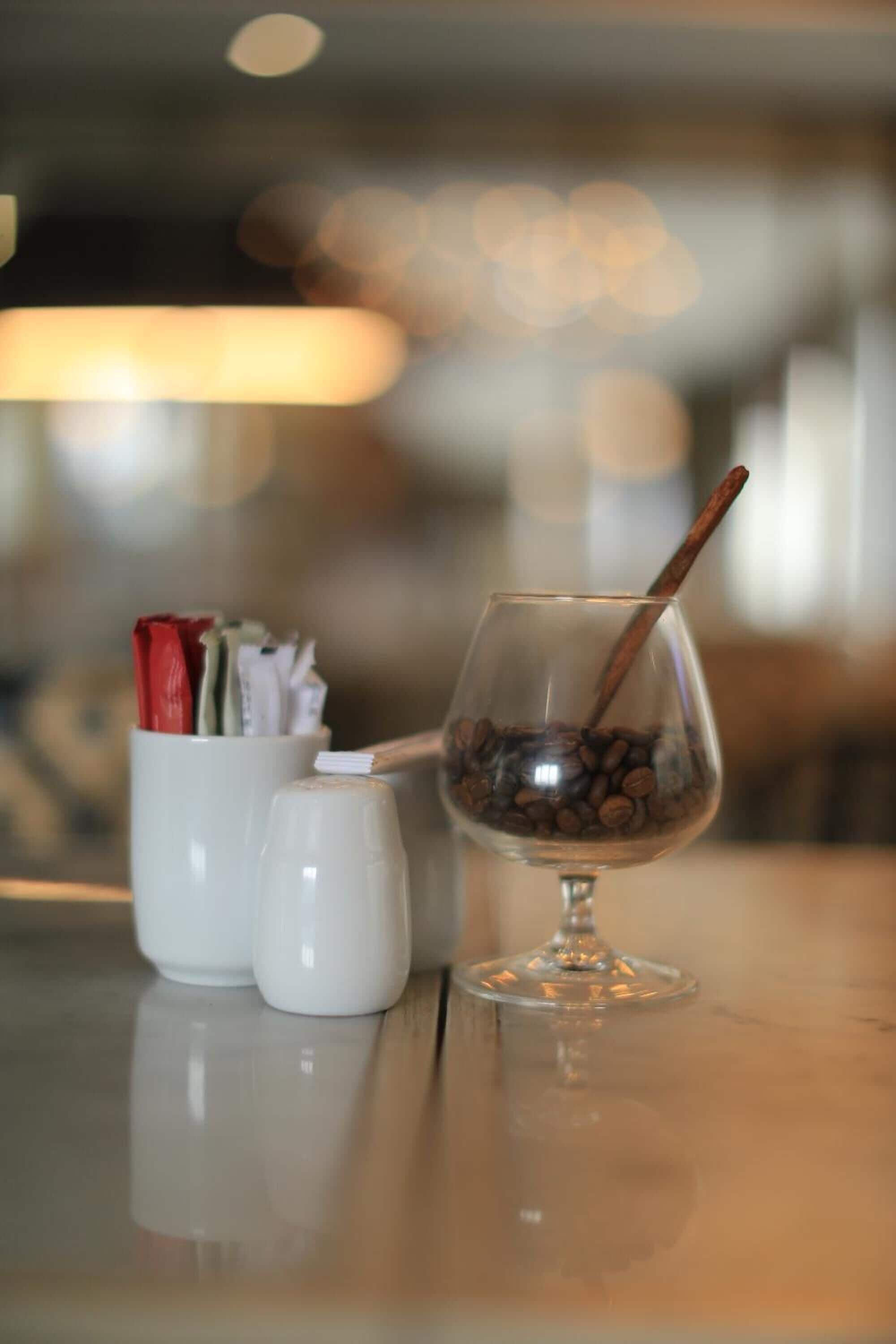 A glass with coffee beans and a cinnamon stick on a table.