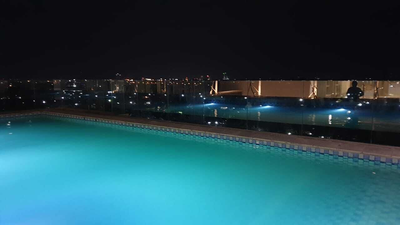 Vista nocturna de una piscina con luces de ciudad al fondo.