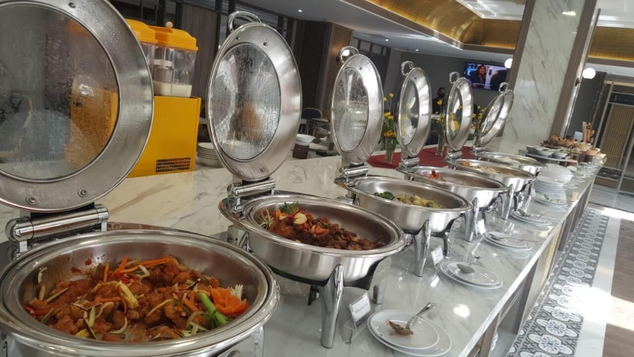 A buffet setup with various food items in metal serving dishes, arranged on a marble counter.