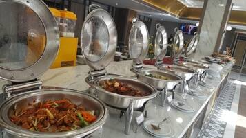 A buffet setup with various food items in metal serving dishes, arranged on a marble counter.