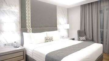 Una habitación de hotel moderna con una cama grande, mesitas de noche, una silla y una ventana con cortinas.