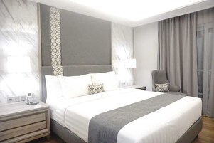 Una habitación de hotel moderna con una cama grande, mesitas de noche, una silla y una ventana con cortinas.