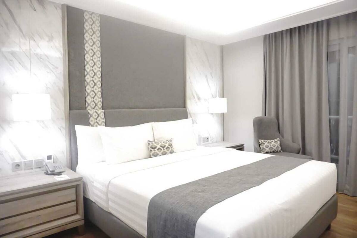 A hotel room with a large bed, bedside tables, a chair, and a window with curtains.