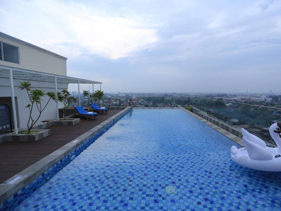Una piscina infinita en la azotea con un flotador con forma de cisne, sillas de descanso y vistas panorámicas de la ciudad.