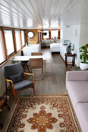 Un interior compacto y moderno con comedor, sofá, una mesita y un ventanal amplio.