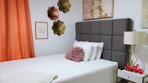 Une chambre à coucher comprenant un lit, un ventilateur de plafond, une table de chevet et des œuvres d’art décoratives au mur.
