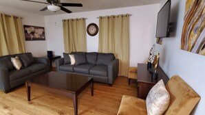 Un salon avec un canapé gris foncé, une table basse en bois et un téléviseur posé sur un meuble.