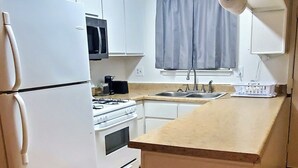 Une cuisine de taille réduite, dotée d’appareils électroménagers blancs, d’un four à micro-ondes, d’une cuisinière et d’un évier.