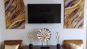 Un salon comprenant deux fauteuils, une console en bois agrémentée d’objets décoratifs et un téléviseur à écran plat fixé au mur.