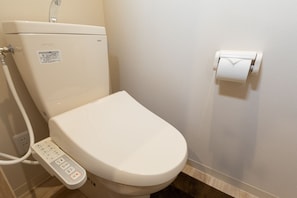 A modern toilet with a control panel, a toilet paper holder, and a visible water pipe. - Experience Sapporo (Sapporo)