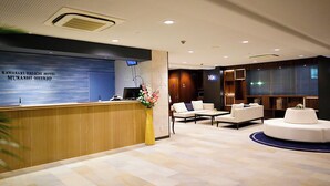 Zona de recepción de hotel con un mostrador de madera, una pared azul decorada con un mural de un paisaje urbano y un área de estar con sofás y una mesa redonda.