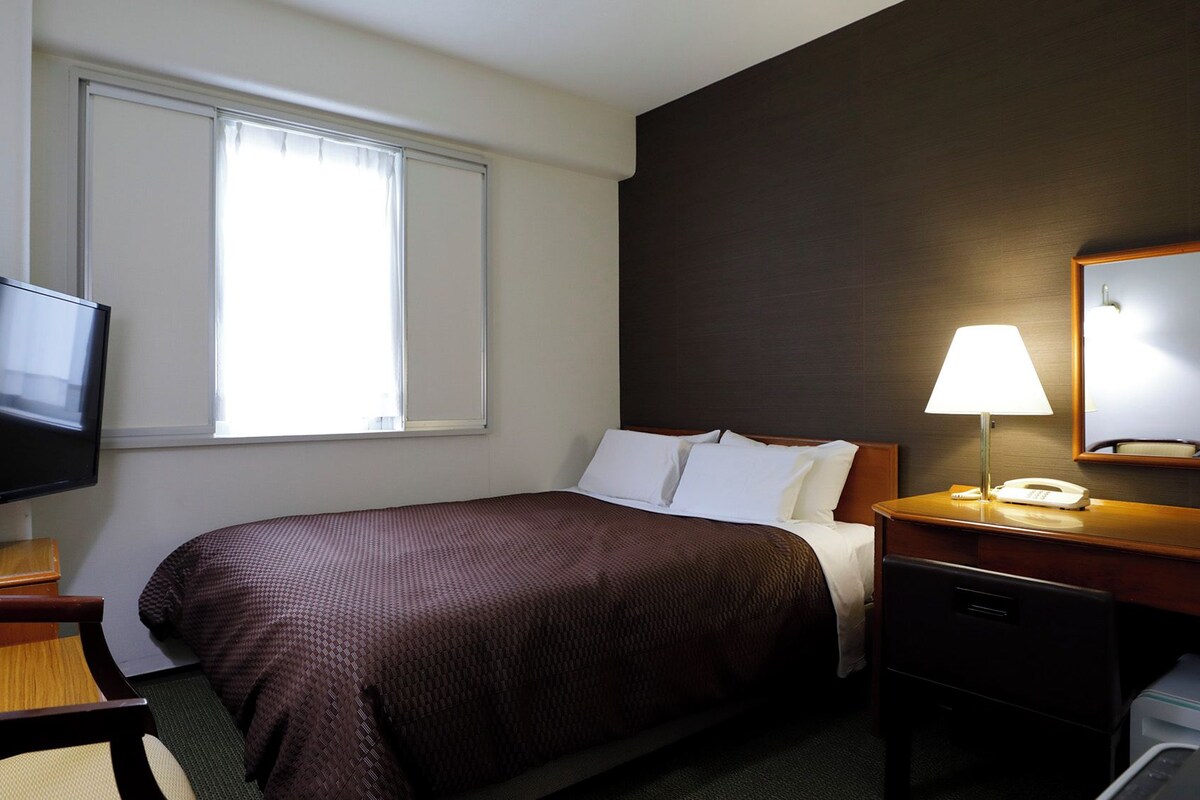 Habitación de hotel con cama, televisión, escritorio con lámpara y teléfono.