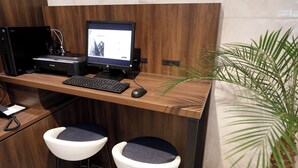 Un escritorio moderno de oficina con una computadora de escritorio, un monitor, un teclado y un ratón. Hay dos sillas blancas con cojines azules. Se ve una planta en maceta a la derecha.