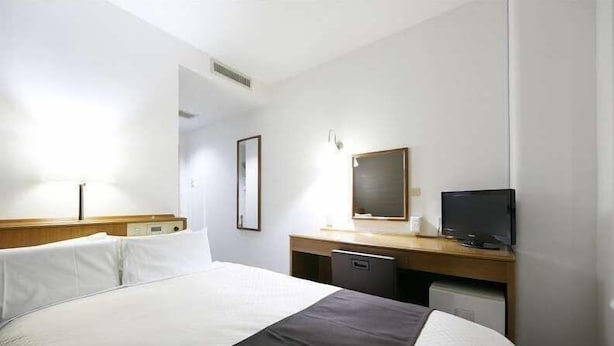 Una habitación de hotel con cama, escritorio y televisión, además de un espejo.