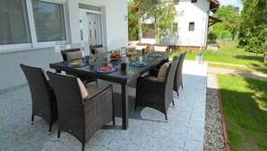 An outdoor dining area with a glass table and wicker chairs, surrounded by a white building with a wooden pergola. - Vacation home Pixie by Interhome (Balatonoszod)