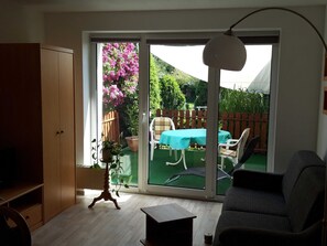 A room with a sliding glass door leading to a patio with a table and chairs, a wooden cabinet, and a small table with a plant.
