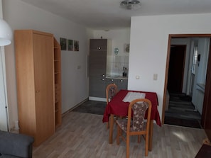 Ein Essbereich mit Tisch für zwei Personen, ein Holzschrank, eine Küche mit gefliestem Spritzschutz und ein Gang, der in einen weiteren Raum führt.