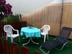 A round table with a light blue tablecloth, two white plastic chairs, a black folding chair, and a potted plant with purple flowers.