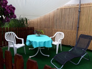 A round table with a light blue tablecloth, two white plastic chairs, a black folding chair, and a potted plant with purple flowers. - Apartment am Klinikum - Apartments am Klinikum (Dessau-Roßlau)