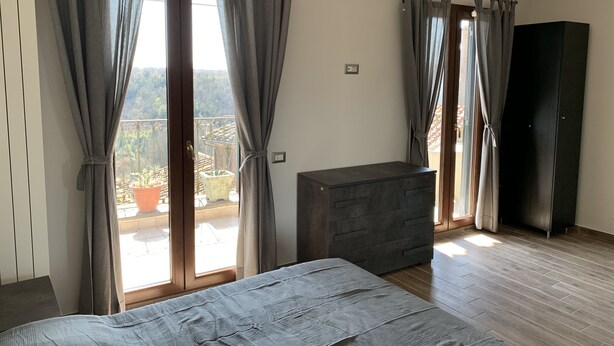 A bedroom with a bed, a dresser, an air conditioner, and a balcony with potted plants. - Alloggio Turistico Belvedere Gallese (Gallese)