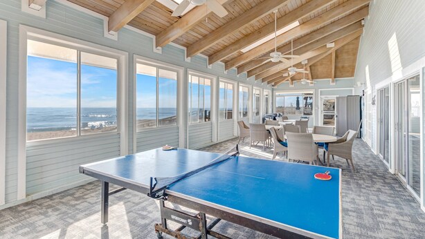 Amplia habitación con mesa de ping pong, ventanas grandes y vista al océano.