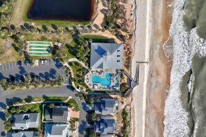An aerial view of a coastal property with a swimming pool, beach access, and a parking area.