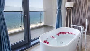 Un baño moderno con una bañera independiente, un amplio ventanal con vista al mar y una lámpara de pie.
