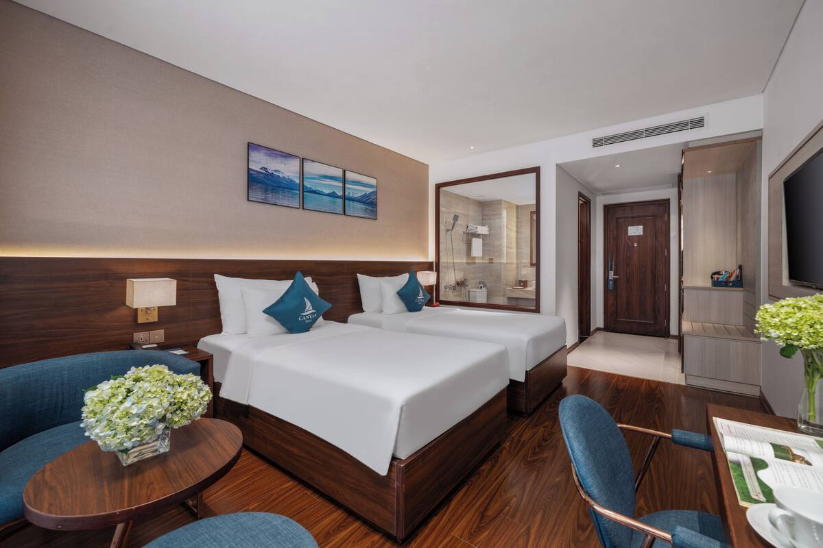 A hotel room with two beds, a sitting area with a table and chairs, a large mirror, and a view of the bathroom.