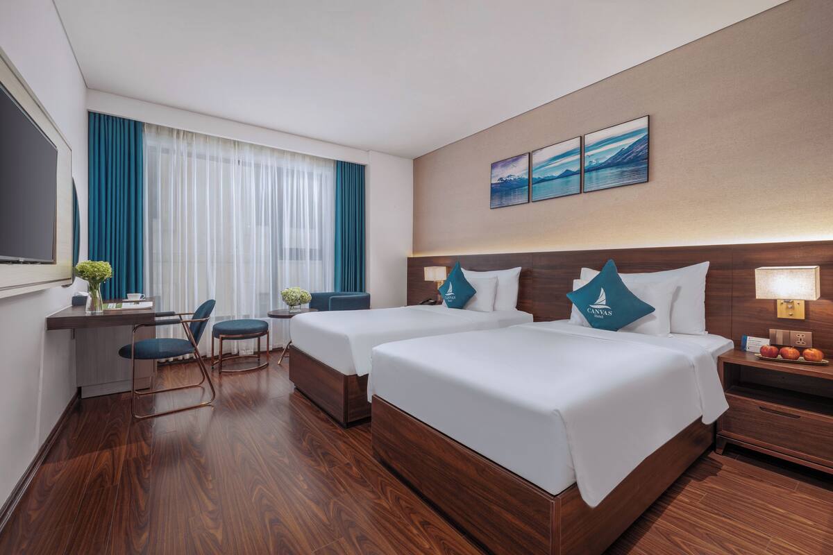 A hotel room with two beds, a desk, a chair, and a TV.