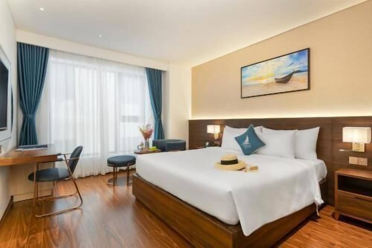 A hotel room with a large bed, a desk, a chair, and a painting on the wall.