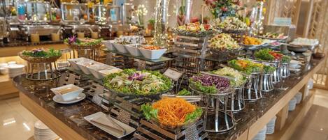 A buffet with various food stations, including salads, vegetables, and other dishes, arranged on a marble counter with a wooden base.