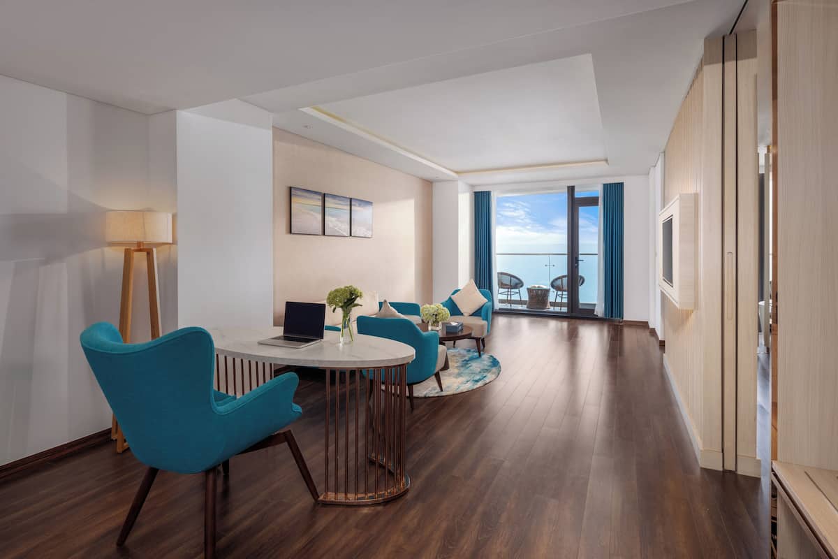 A modern hotel room with a dining area, a sofa set, a TV, and a view of the sky.