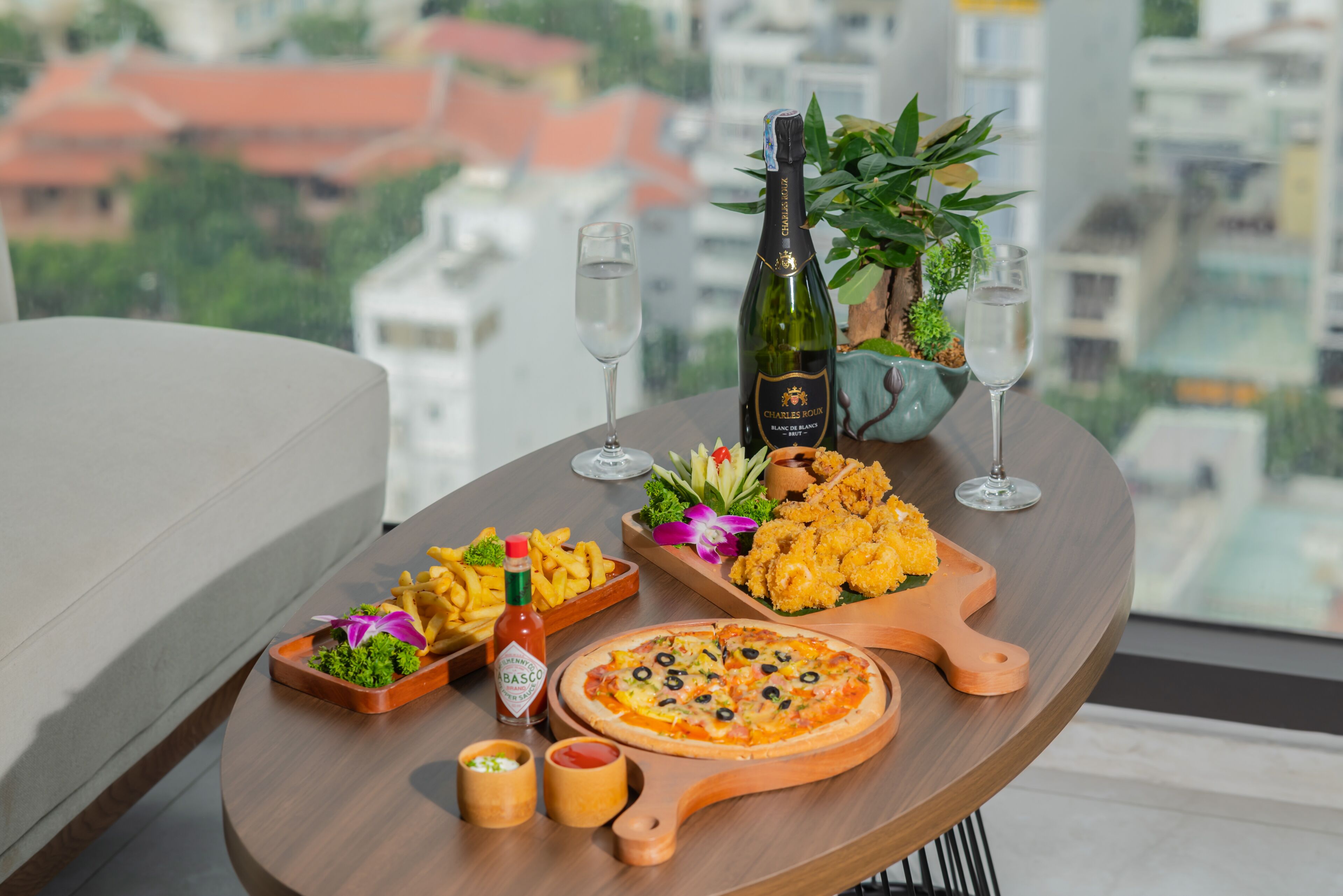Una mesa con pizza, calamares fritos y una botella de champán, con vista a la ciudad.