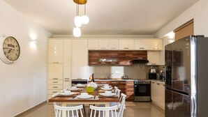Une cuisine moderne avec un coin repas, comprenant une table en bois, des chaises blanches, un réfrigérateur en acier inoxydable et des armoires en bois.