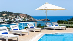 Un espace aménagé au bord de la piscine, avec des chaises longues et un grand parasol, offrant une vue sur le paysage côtier.