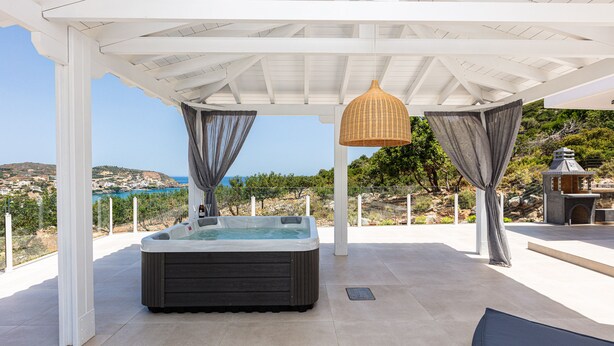 Un bain à remous sous une pergola blanche, avec vue sur la mer.
