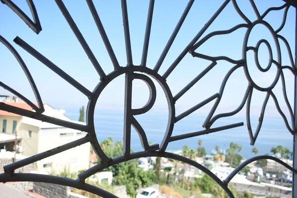 Une grille en métal ornée d’un motif rappelant un soleil, avec un grand « R » bien visible, surplombe une zone résidentielle côtière, avec ses maisons et son ciel dégagé.