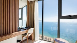 A modern hotel room with a large window offering a sea view, a wooden desk, a chair, and a small table. - Masova Hotel (Nha Trang)