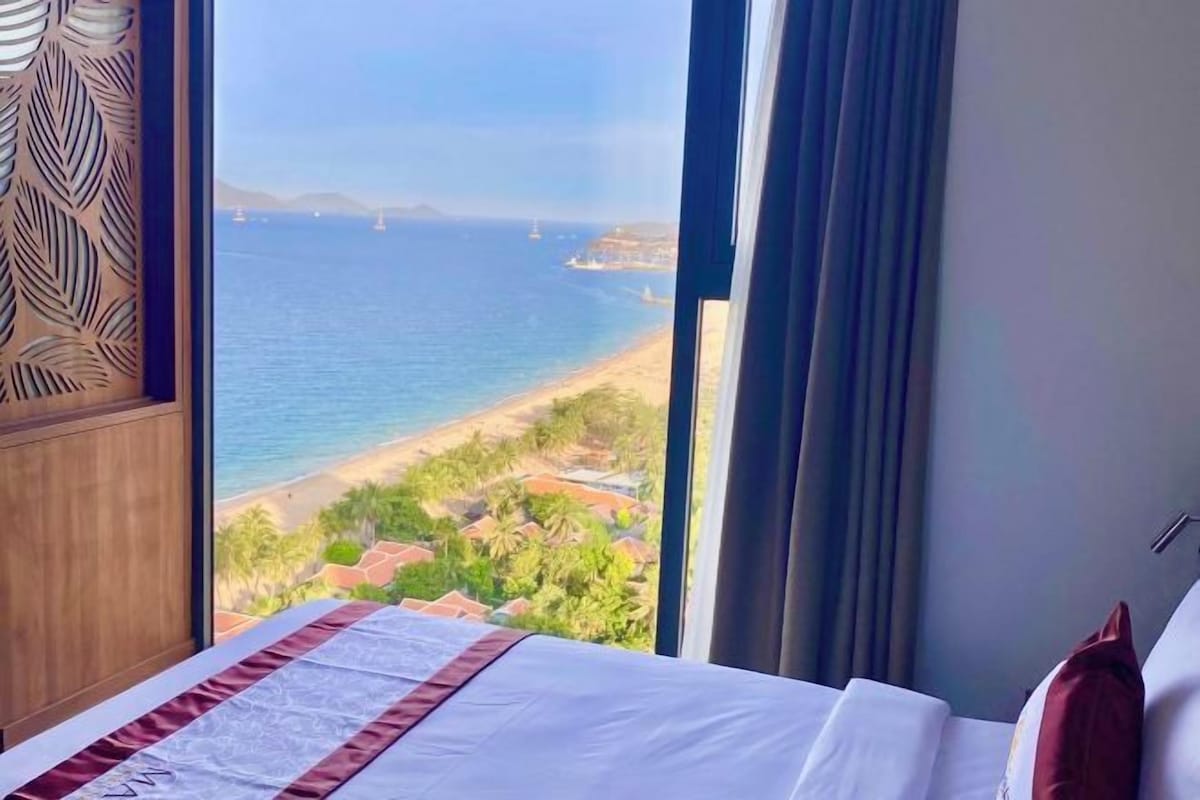 Een hotelkamer met een groot raam met uitzicht op zee en een strand.