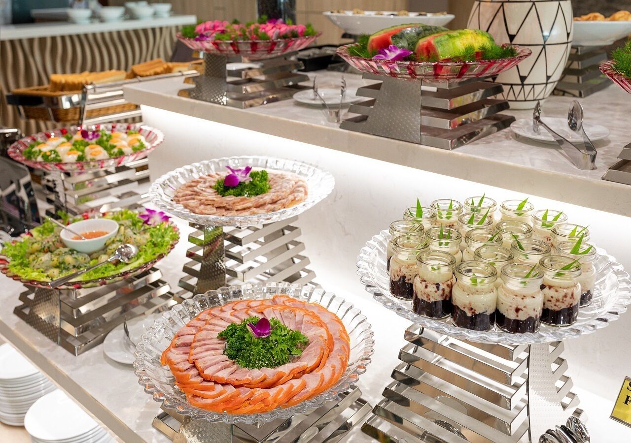 A buffet with various dishes including a large platter of sliced meat, a salad, and small jars of dessert.