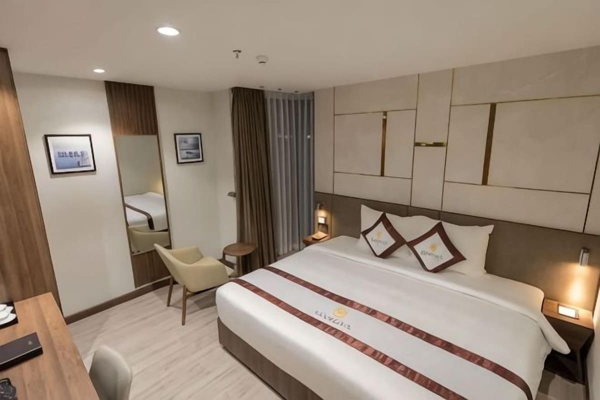 Een hotelkamer met een groot bed, nachtkastjes, een bureau, een stoel en uitzicht op de stad.
