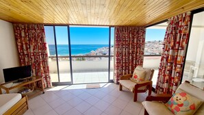 Ein Balkon mit Fernseher, Stühlen und Blick auf das Meer und die Gebäude.