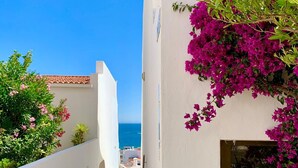 Ein schmaler, weiß gekachelter Korridor mit Fliesenboden führt zu einem Balkon mit Blick auf das Meer.