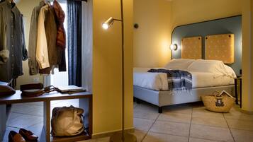 Una camera d'hotel con un letto, un comodino, una lampada e un armadio pieno di vestiti.