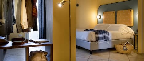 A hotel room with a bed, bedside table, lamp, and a wardrobe with hanging clothes.