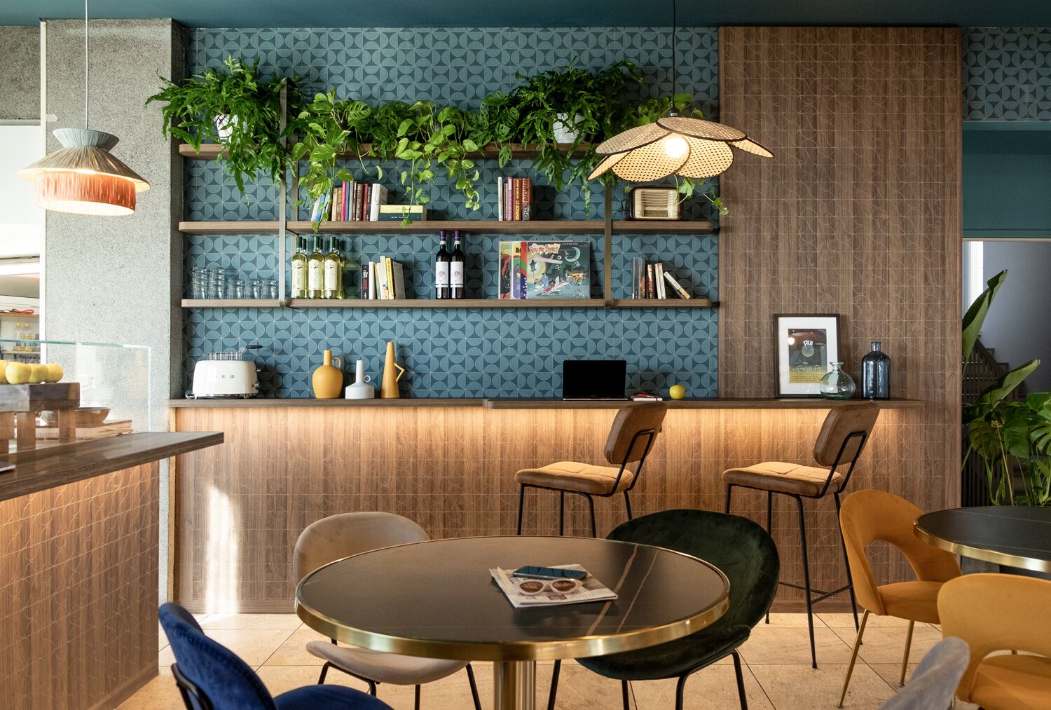 Zona de bar moderna con una mesa redonda, taburetes y una estantería llena de libros y botellas.