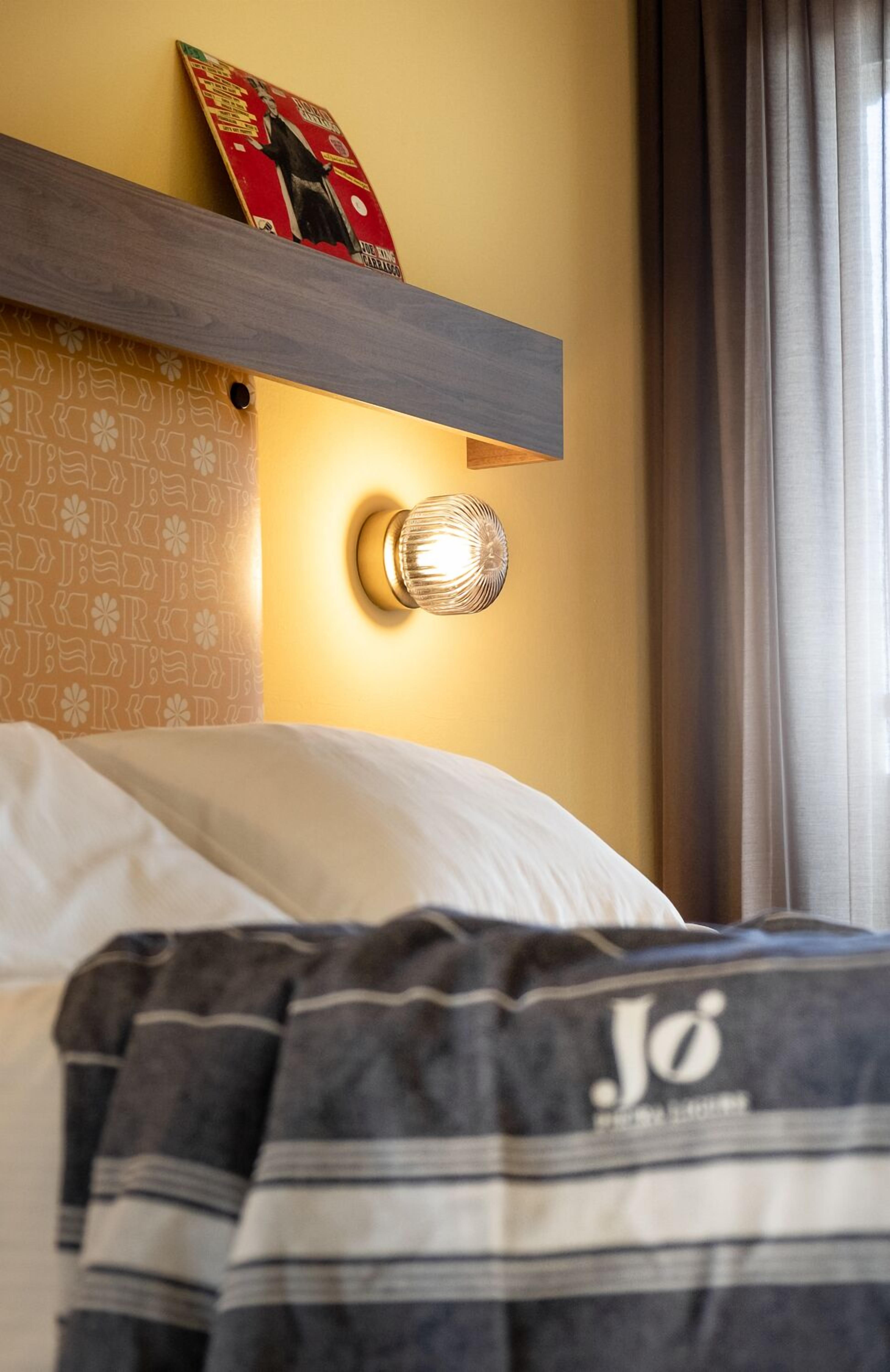 Quarto de hotel com cama, luminária na parede e quadro emoldurado sobre a cama.